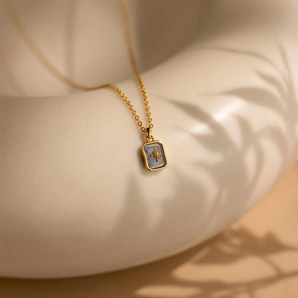 North Star Birthstone Necklace in Aquamarine for March, featuring a rectangular crystal pendant resting on a round white surface and casting soft shadow patterns.
