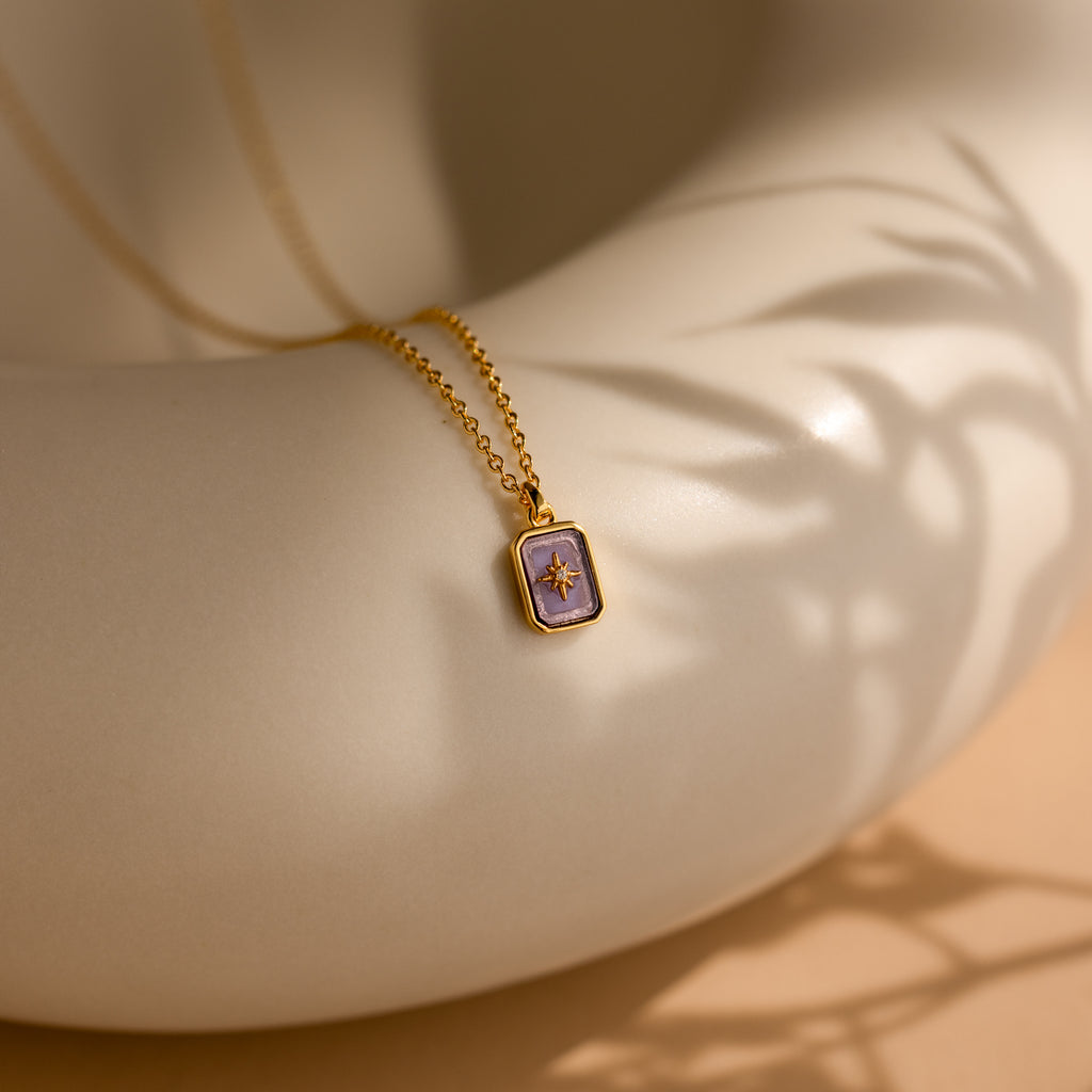 The North Star Birthstone Necklace in Alexandrite (June) rests elegantly on a smooth, cream-colored curved surface, showcasing its radiant charm.