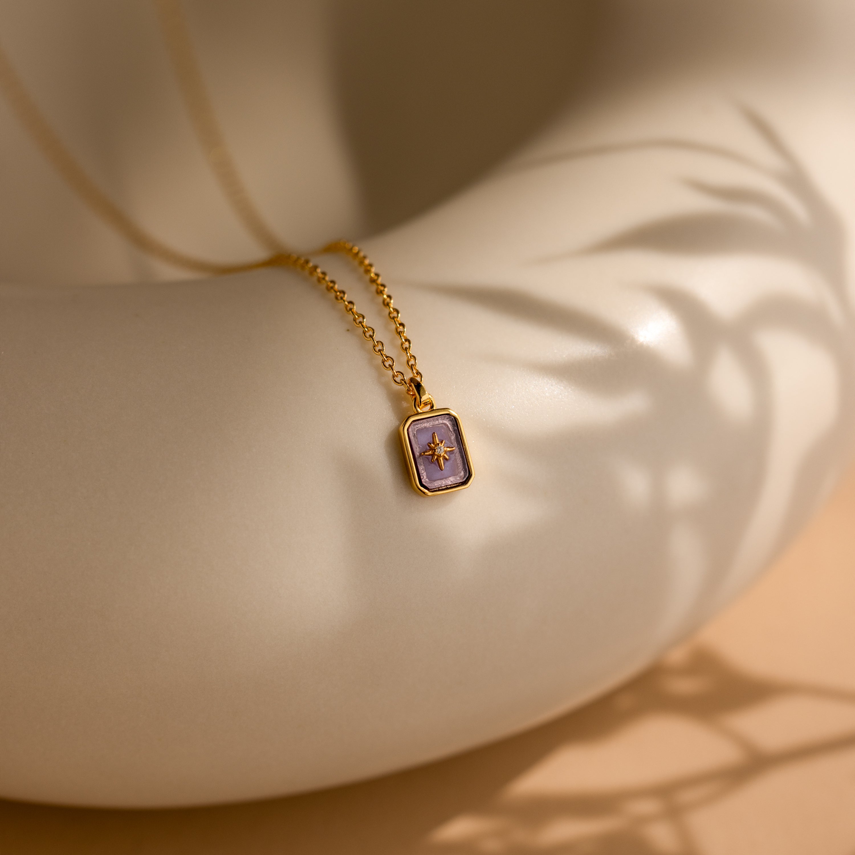 The North Star Birthstone Necklace in Alexandrite (June) rests elegantly on a smooth, cream-colored curved surface, showcasing its radiant charm.
