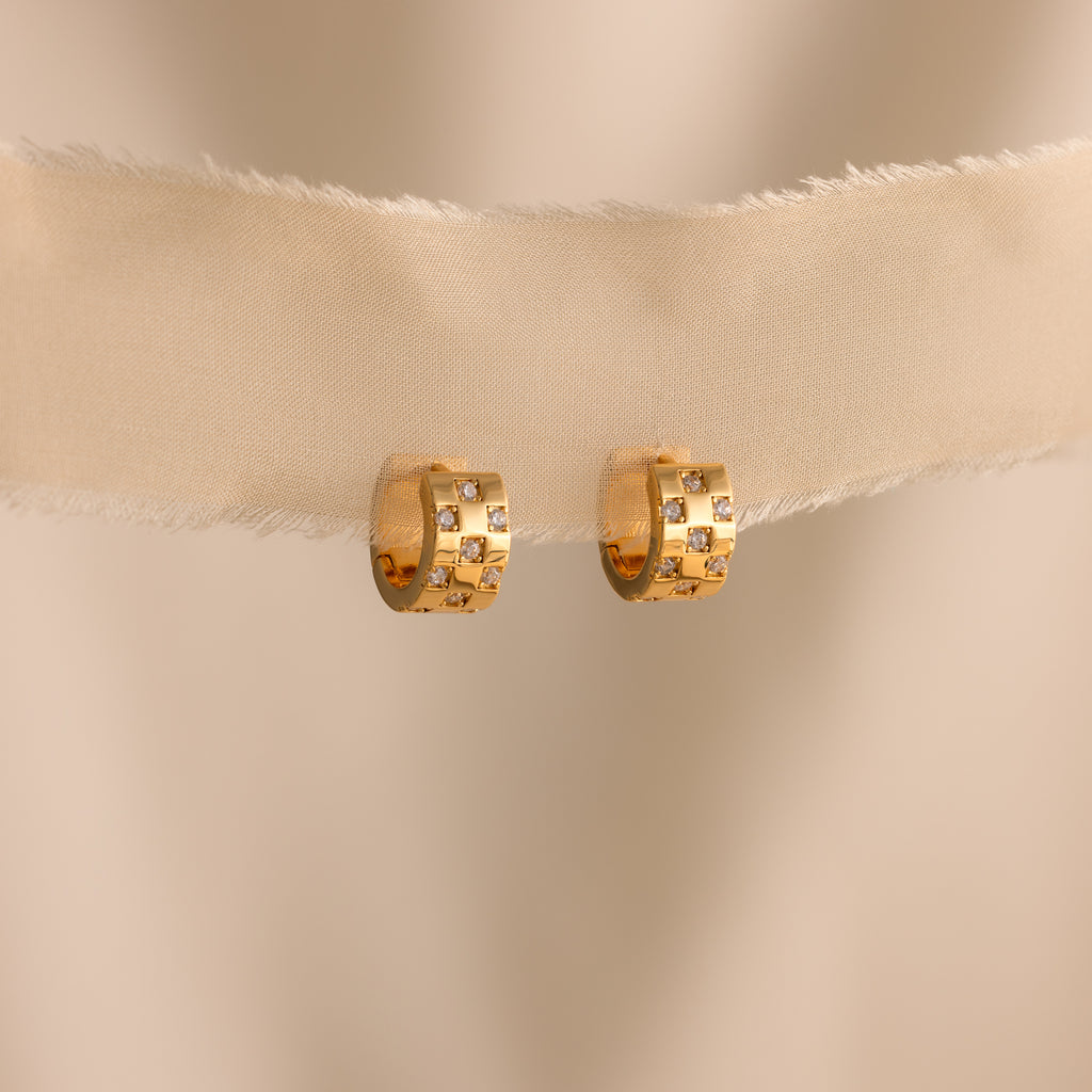 Pave Checkered Huggies—gold hoop earrings with small square diamond accents—displayed on beige fabric against a neutral background.