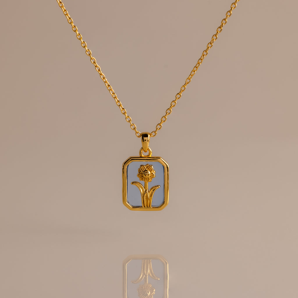 Aquamarine Birth Flower Charm Necklace: gold necklace with a rectangular pendant featuring a floral design, displayed on a light background.
