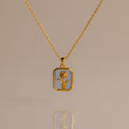 Aquamarine Birth Flower Charm Necklace: gold necklace with a rectangular pendant featuring a floral design, displayed on a light background.