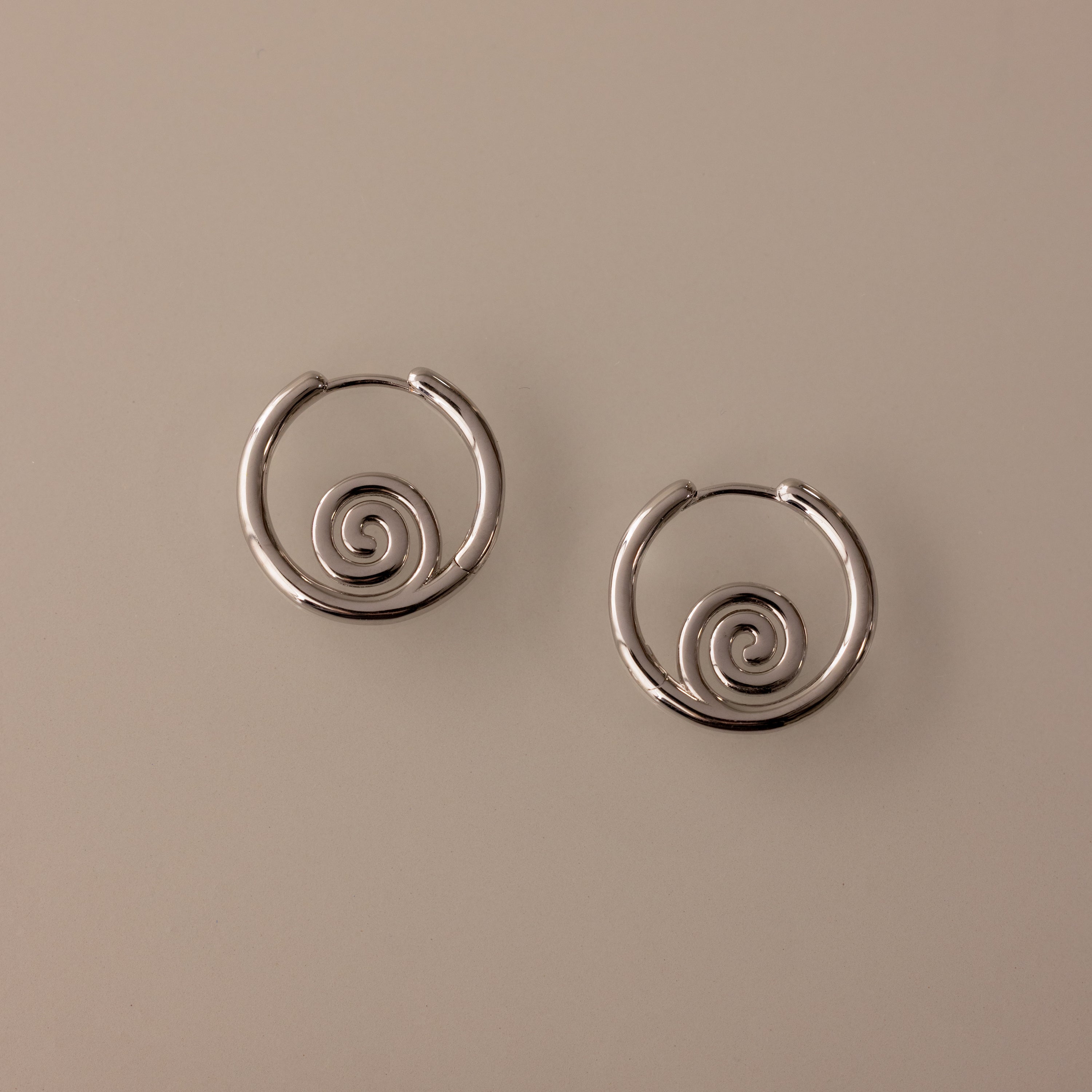 Spiral Swirl Hoops in Silver with intricate spiral designs rest on a light beige background—perfect boho earrings for your next beach vacation jewelry collection.