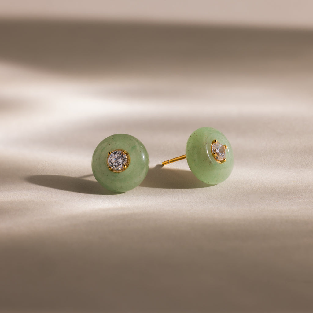 Close-up of round green jade stud earrings featuring a sparkling CZ diamond center and gold bezel setting, displayed on a neutral background.