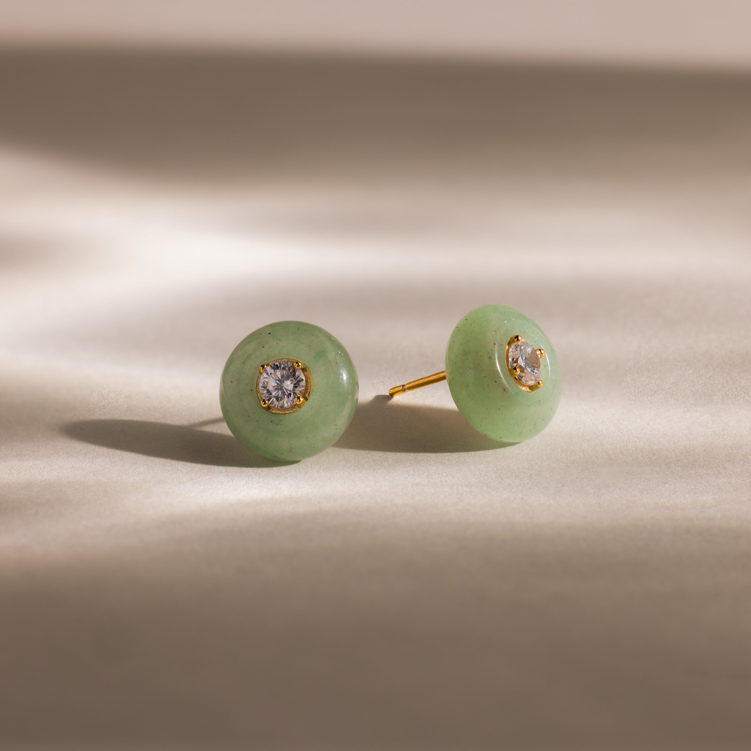 Close-up of round green jade stud earrings featuring a sparkling CZ diamond center and gold bezel setting, displayed on a neutral background.