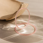The Thin Pink Jade Bangle Set features two translucent pink jade bangles displayed on a light surface beside a beige ceramic bowl—ideal for effortless layering.