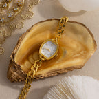 The Heirloom Chain Link Timepiece, featuring a mother of pearl dial, is showcased on an open oyster shell with a gold-trimmed edge.