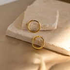 The Medium Bold Hoops are stylish gold earrings, lightweight and perfect for everyday wear, shown on textured beige stone slabs with a soft neutral background.