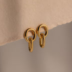 Twisted Link Earrings in 18K Gold showcase an oval, textured chain design against a soft beige background—ideal for those who love modern and elegant jewelry.