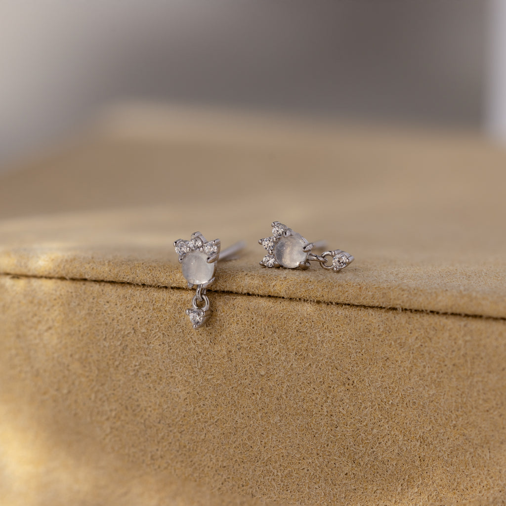 Halo Moonstone Drop Studs in Sterling Silver showcase royal elegance with their teardrop-shaped stones, beautifully displayed on a light tan velvet surface.