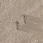 The Halo Moonstone Drop Studs in Sterling Silver exude royal elegance, their star-inspired design shimmering beautifully on a textured, light surface.