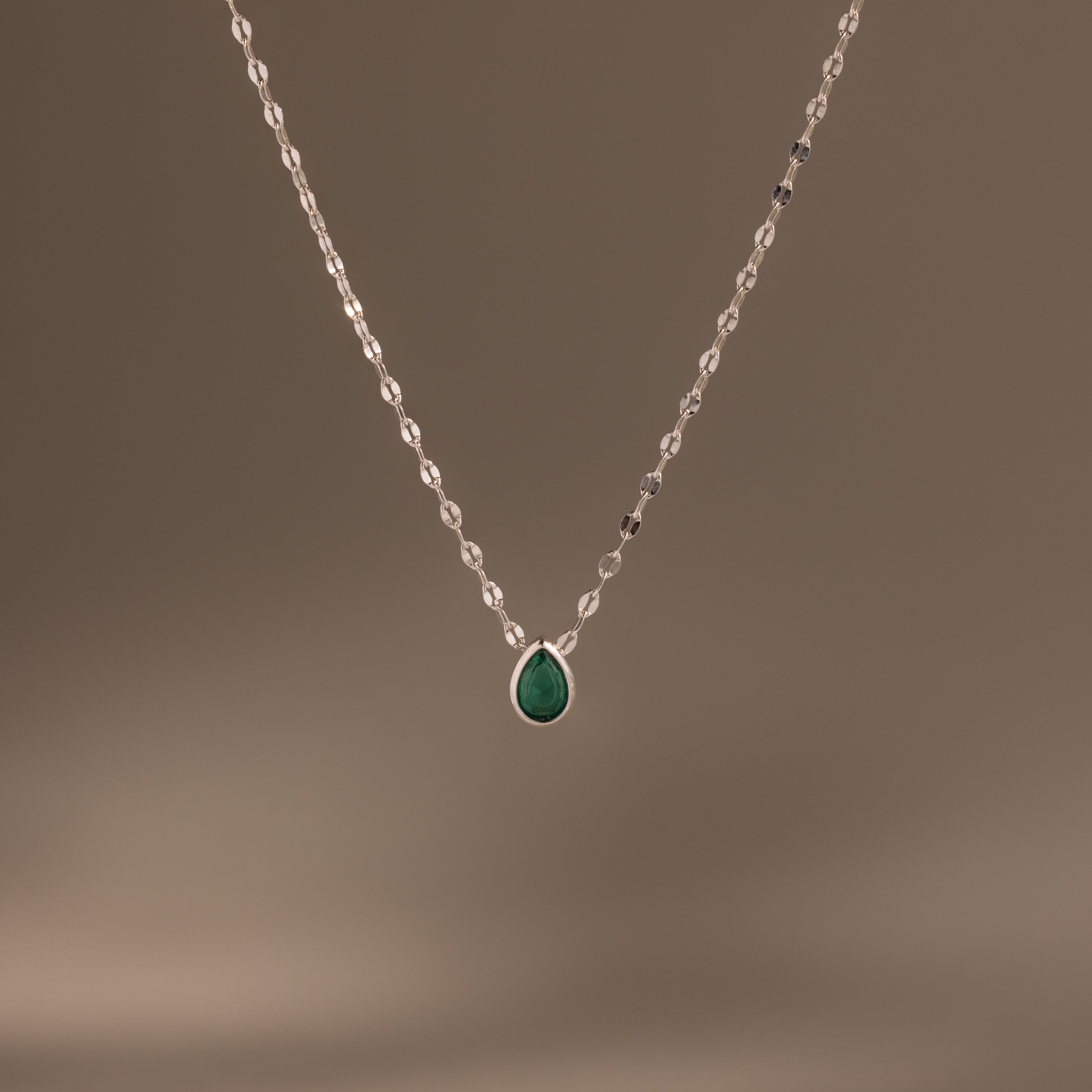 Multiple Teardrop Birthstone Necklace featuring a delicate silver chain and small green pendant, shown on a plain brown background—ideal as personalized jewelry or a meaningful gift.
