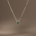 The Multiple Teardrop Birthstone Necklace in Sterling Silver features a delicate chain with small green pendants, displayed on a plain beige background—an elegant keepsake jewellery piece ideal for everyday wear.