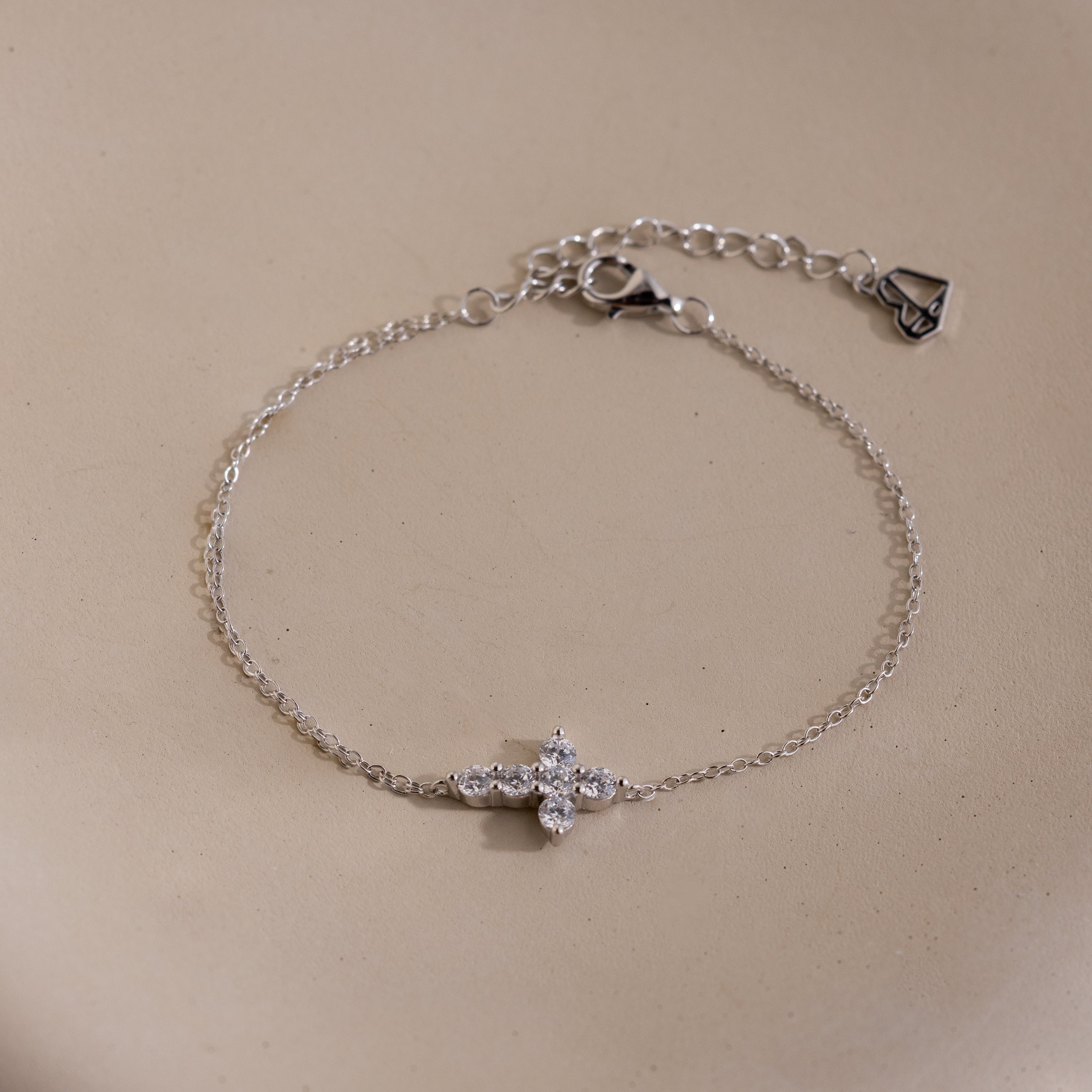 Silver chain bracelet with an adjustable clasp, featuring a cross shaped charm set with small round white gemstones.