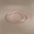 The Thin Pink Jade Bangle Set features two slim, light pink bangles that overlap elegantly on a cream surface—ideal for creating a delicate layered bracelet look.