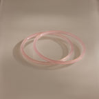 The Thin Pink Jade Bangle Set features two slim, light pink bangles that overlap elegantly on a cream surface—ideal for creating a delicate layered bracelet look.