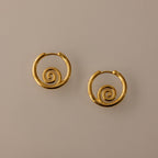 The Spiral Swirl Hoops in 18K Gold feature intricate spiral designs, making them perfect boho vacation jewelry, shown against a plain beige background.