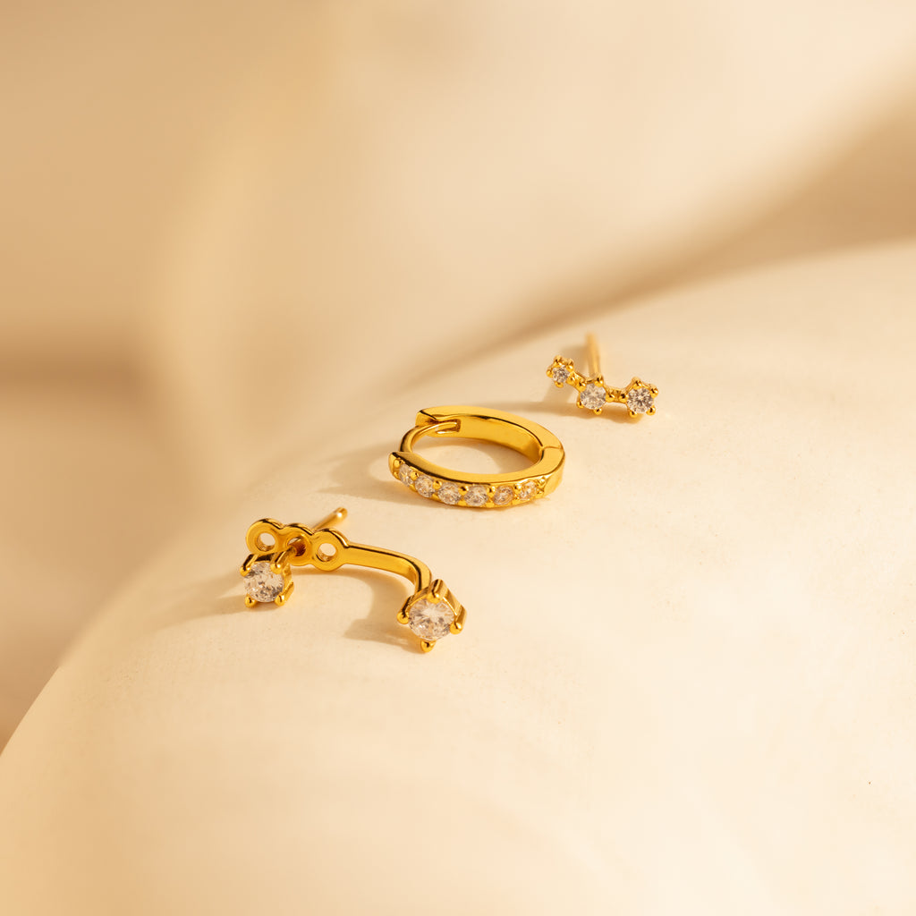 The Diamond Earrings Set features gold pave huggie hoops with small diamonds, beautifully displayed on a soft beige fabric background.
