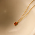 North Star Birthstone Necklace in garnet (January) features a gold chain and rectangular red crystal pendant with a diamond-set North Star design, shown against a beige background.