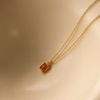 North Star Birthstone Necklace in garnet (January) features a gold chain and rectangular red crystal pendant with a diamond-set North Star design, shown against a beige background.