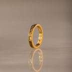 The Peridot Inlay Eternity Ring with gold and decorative patterns stands upright, its gleaming reflection visible on a smooth, neutral surface.
