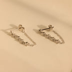 Diamond Chain Drop Earrings in Silver feature delicate chains and small crystals, elegantly displayed on a smooth beige surface.