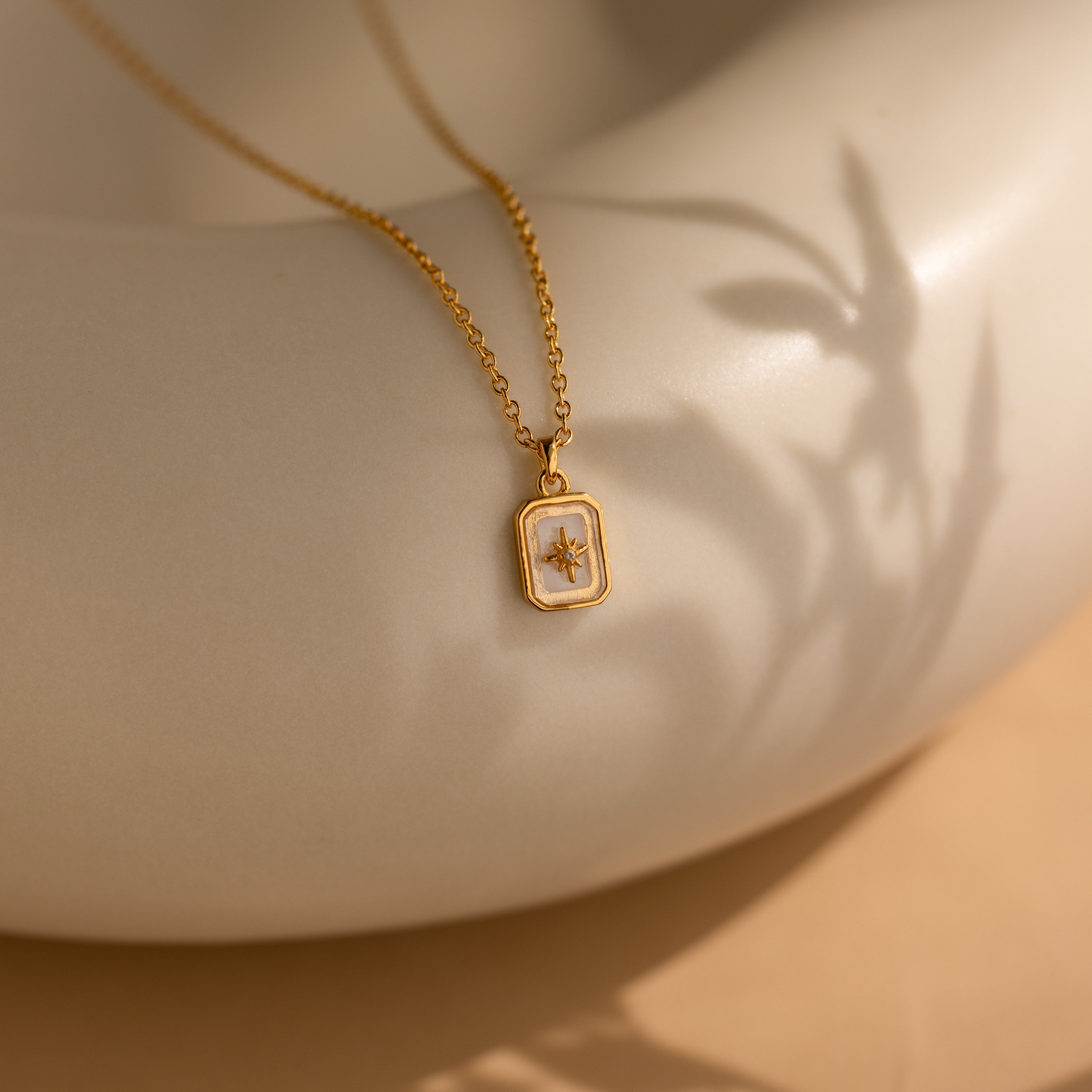 North Star Birthstone Necklace in Diamond / April, featuring a rectangular pendant with a small flower and delicate crystal, displayed on a smooth light surface.