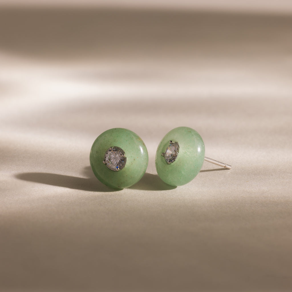Close-up of round green jade stud earrings featuring a sparkling CZ diamond center and silver bezel setting, displayed on a neutral background.
