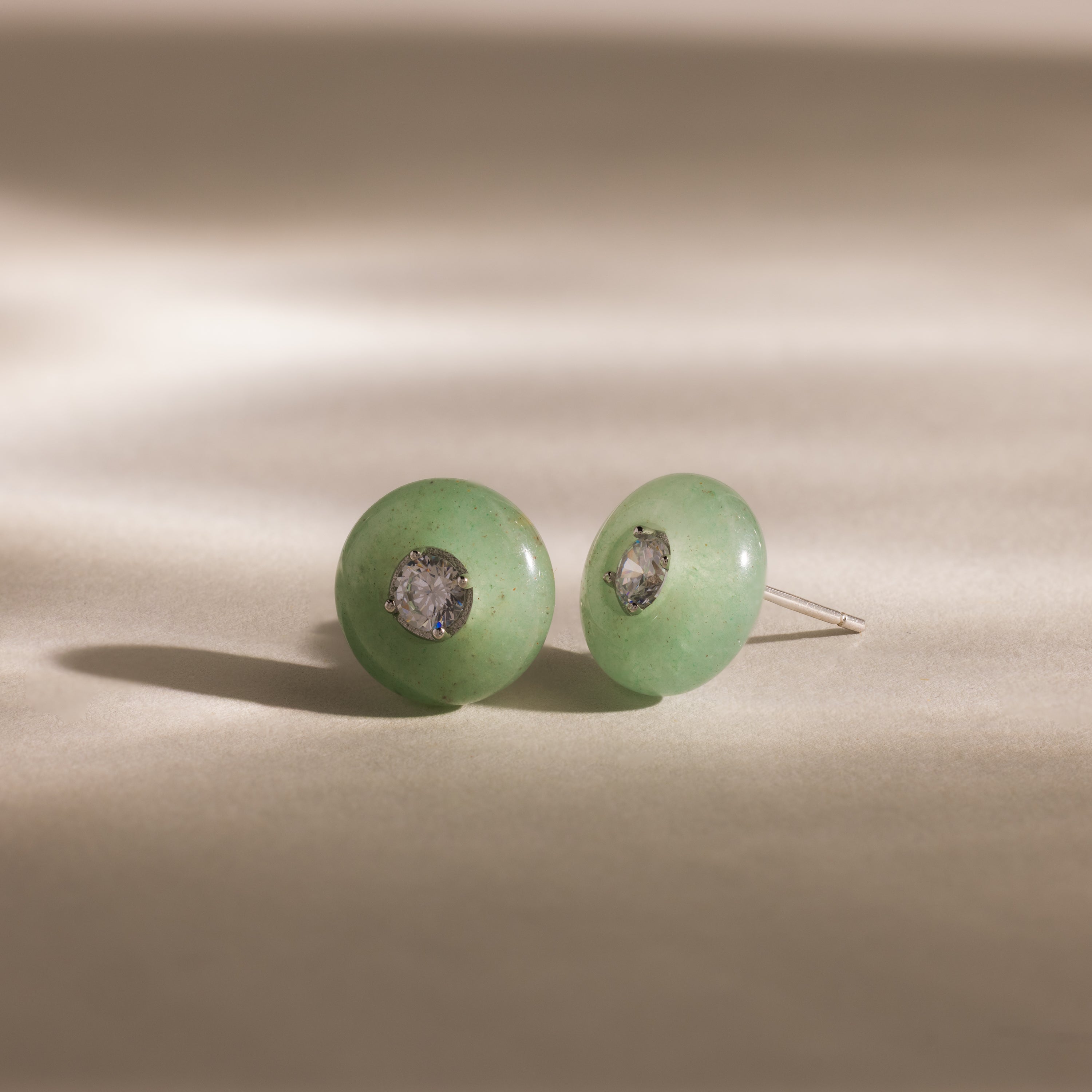 Close-up of round green jade stud earrings featuring a sparkling CZ diamond center and silver bezel setting, displayed on a neutral background.