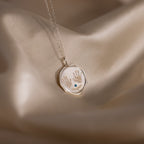 The Baby Hand & Footprint Necklace features engraved handprints, a blue gem, and the name Reagan on satin—perfect personalized baby jewelry for cherished memories.