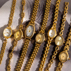 Seven Heirloom Chain Link Timepieces, featuring various designs like diamond accents and mother of pearl dials, are arranged side by side on a patterned background.