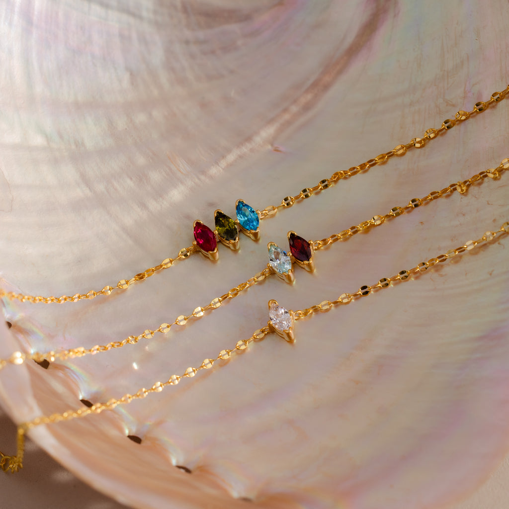 The Multiple Marquise Birthstone Bracelet—a gold chain bracelet with customizable colorful gemstone charms—is beautifully displayed on a pearlescent seashell background, perfect for fans of unique birthstone jewelry.