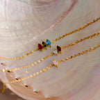 The Multiple Marquise Birthstone Bracelet—a gold chain bracelet with customizable colorful gemstone charms—is beautifully displayed on a pearlescent seashell background, perfect for fans of unique birthstone jewelry.