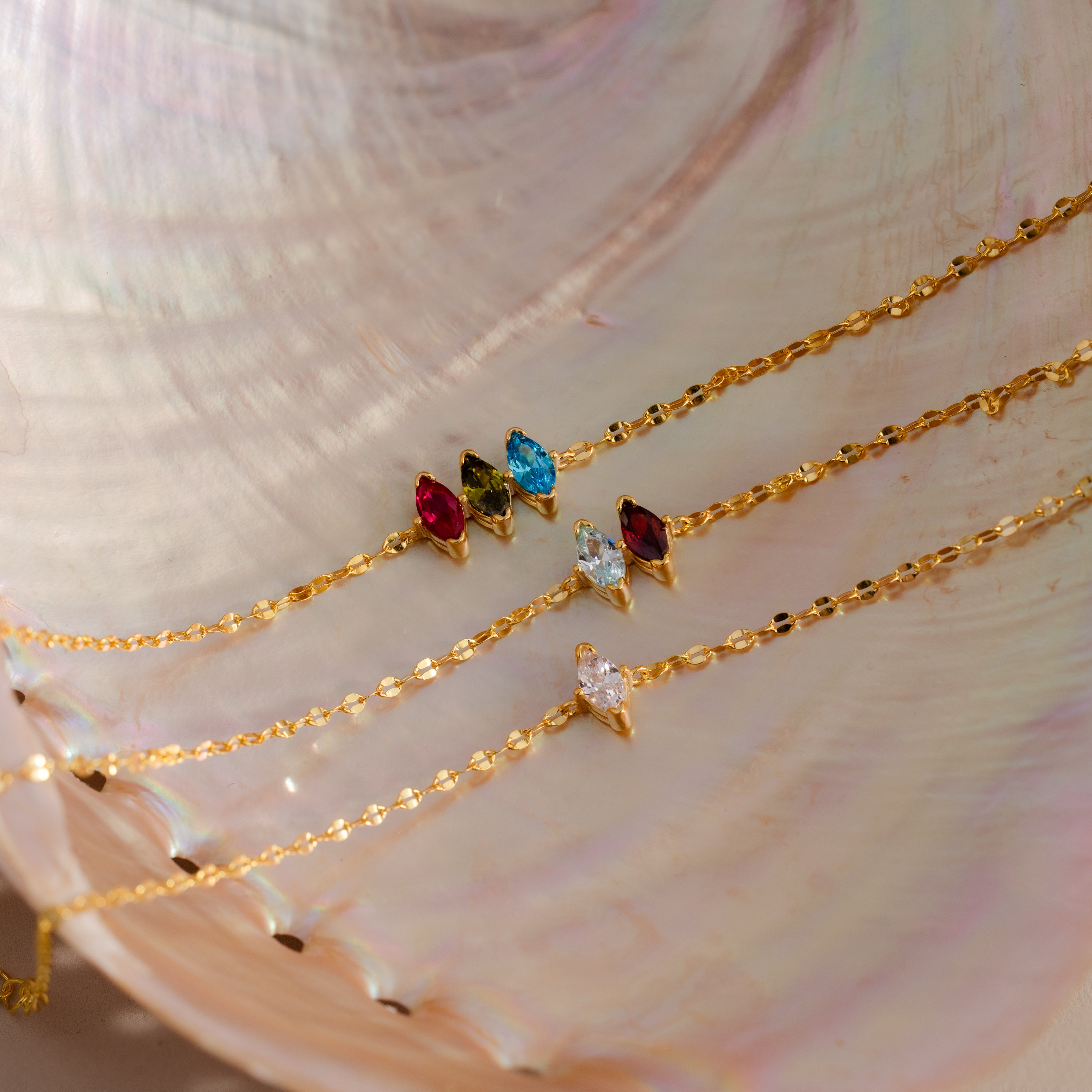 The Multiple Marquise Birthstone Bracelet—a gold chain bracelet with customizable colorful gemstone charms—is beautifully displayed on a pearlescent seashell background, perfect for fans of unique birthstone jewelry.