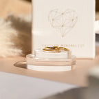The Thin Stacking Rings Set features two gold rings on clear stands with a geometric heart backdrop—ideal as a thoughtful Christmas gift or for beginning your own stylish ring stack.
