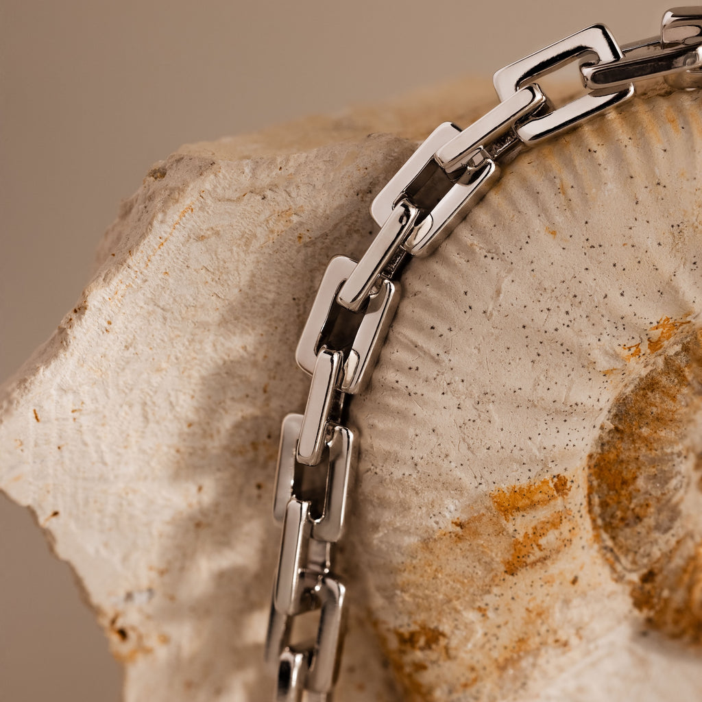 The Eternal Link Bracelet in Silver, a true modern essential, draped over a textured, fossil-like stone background.