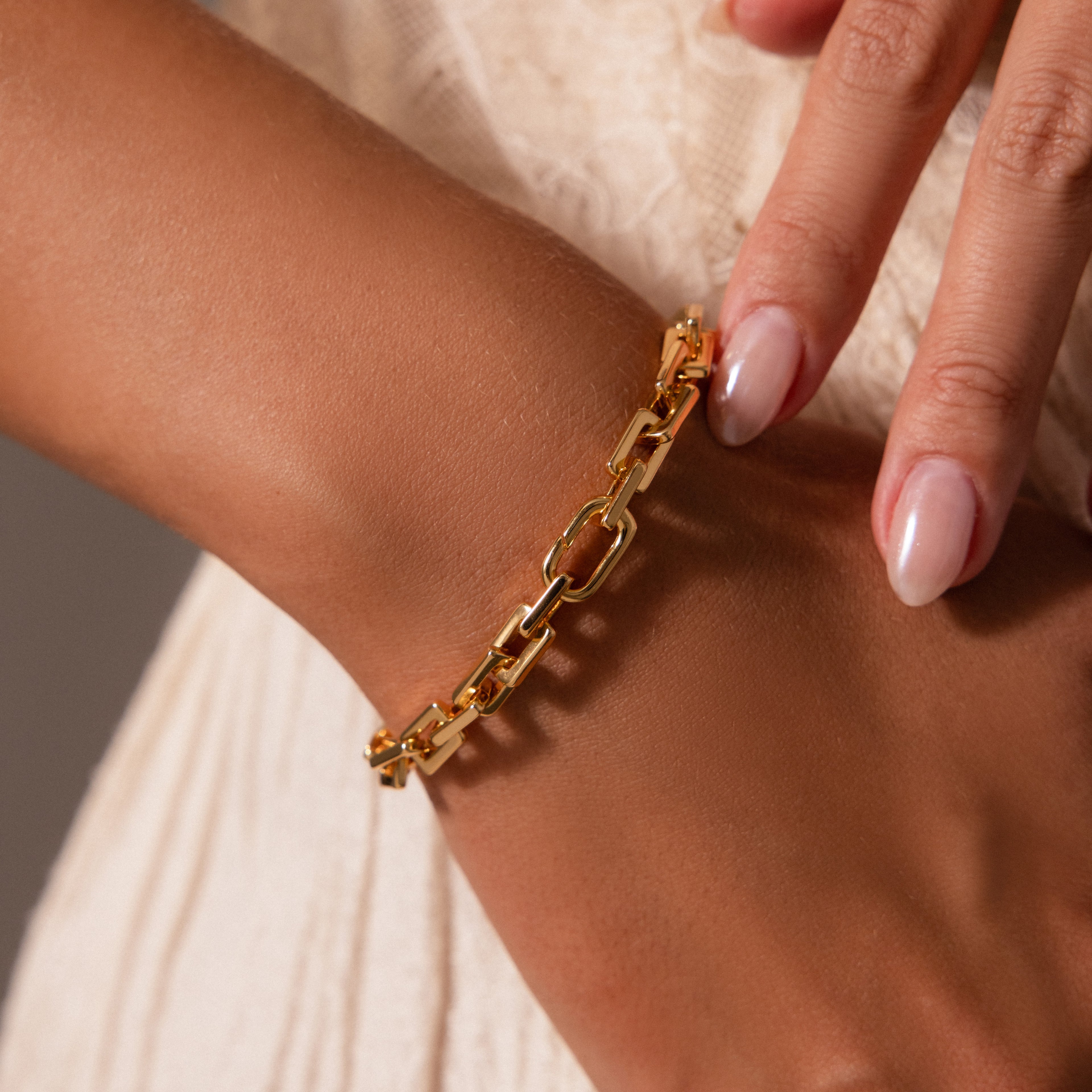 A hand with neatly manicured nails adjusts the Eternal Link Bracelet in 18K Gold, its geometric design showcasing modern essential style.