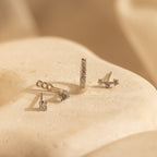 Four delicate silver earrings, featuring a Diamond Earrings Set in Sterling Silver and a sparkling pavé huggie hoop, are displayed on a smooth, cream-colored stone surface.