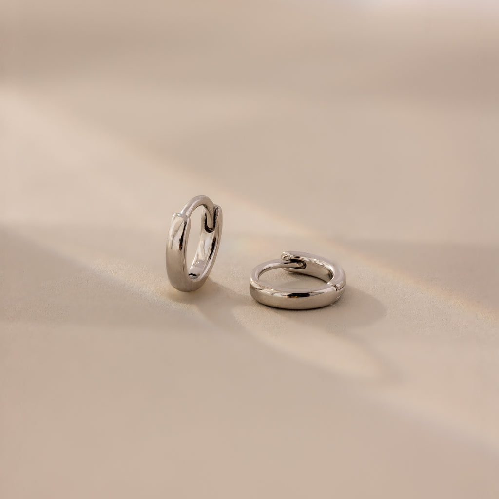 Pair of 6mm tiny classic silver huggie hoop earrings displayed on a neutral satin surface with soft natural lighting.