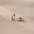 Pair of 6mm tiny classic silver huggie hoop earrings displayed on a neutral satin surface with soft natural lighting.