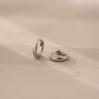 Pair of 6mm tiny classic silver huggie hoop earrings displayed on a neutral satin surface with soft natural lighting.