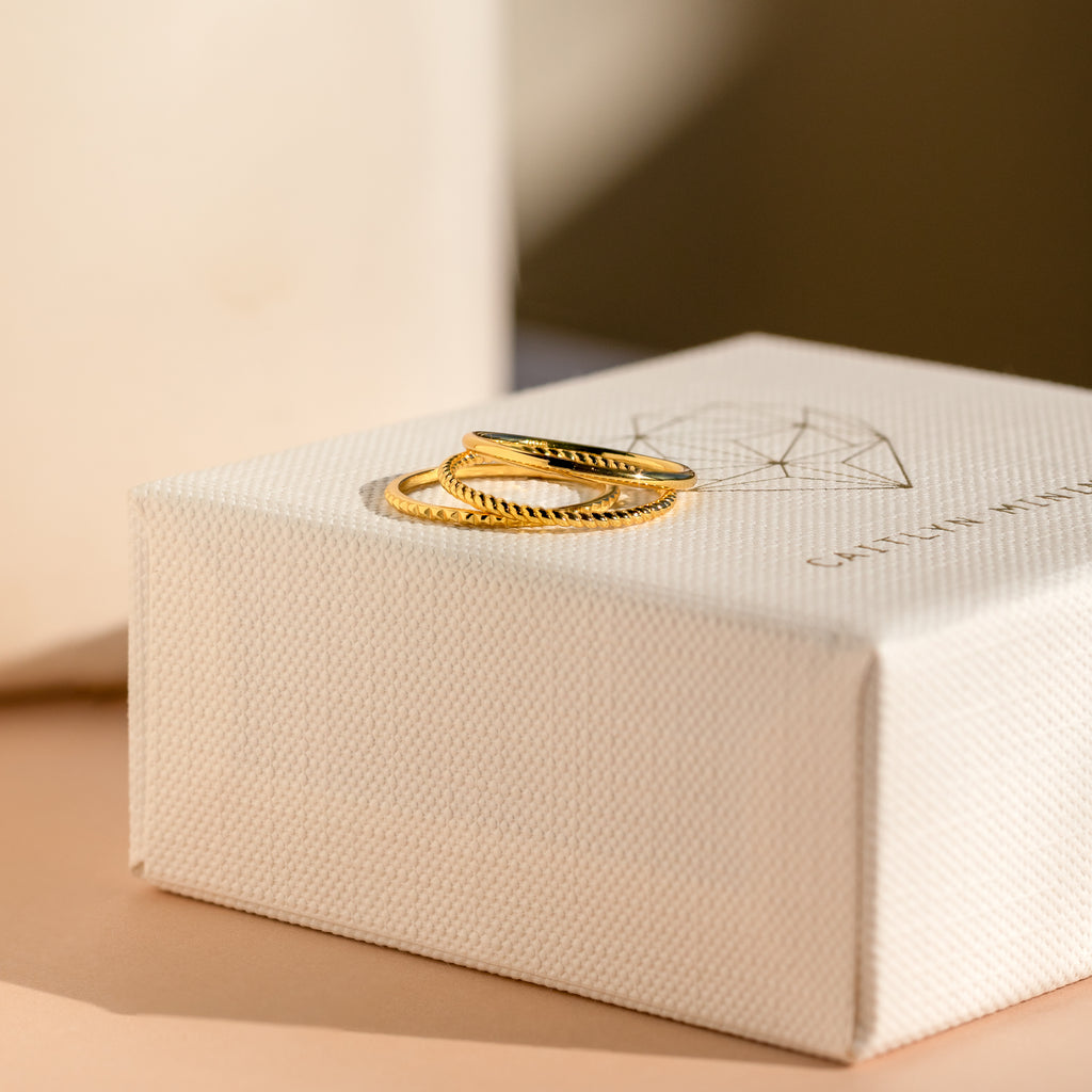 The Thin Stacking Rings Set features two gold rings displayed on a textured white jewelry box in soft natural light—ideal as a Christmas gift or for beginning your own elegant ring stack.