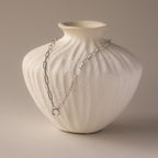 The Paperclip Clasp Necklace in White Gold is elegantly draped over a textured white ceramic vase against a neutral background.