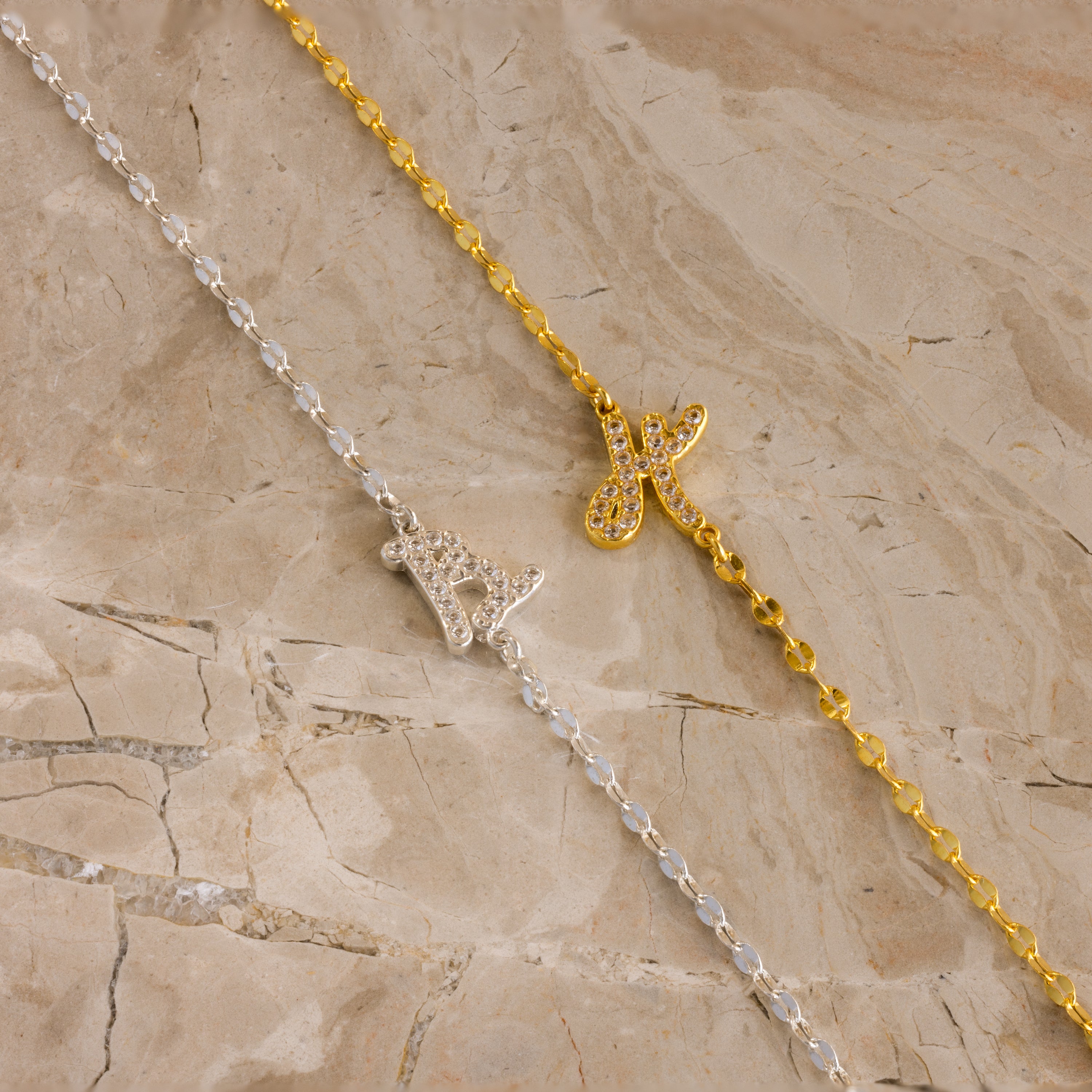 The Nella Pave Off-Center Initial Necklace, shown with K and A pendants in gold and silver on marble, is perfect for adding a personalized touch.