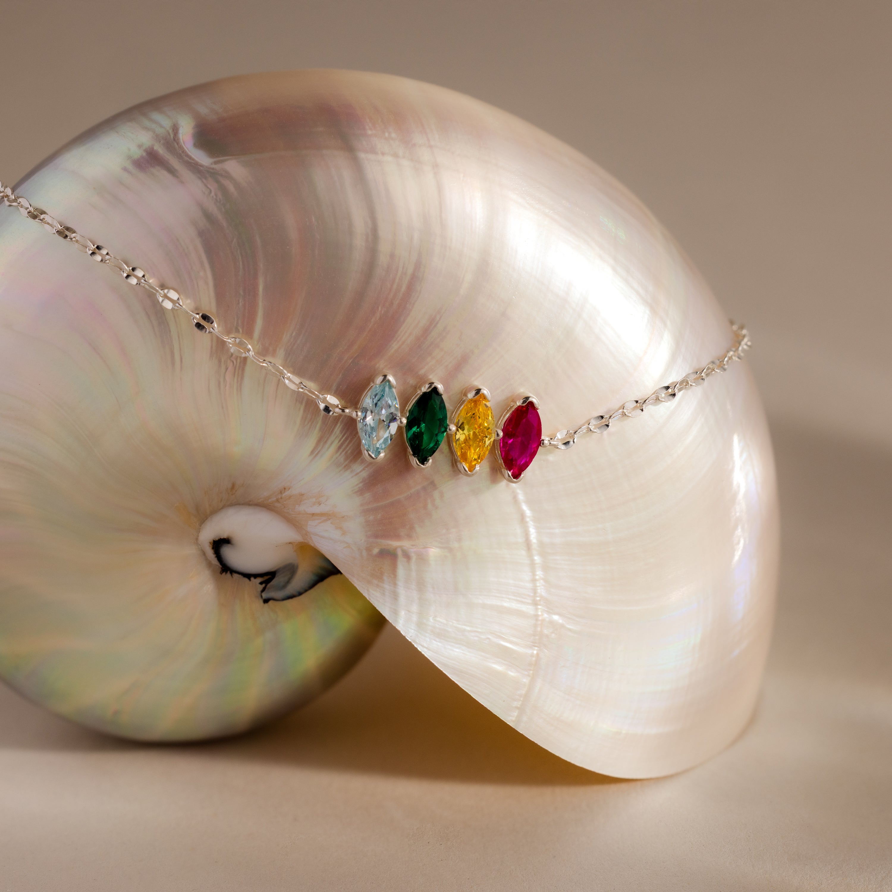 The Multiple Marquise Birthstone Bracelet, featuring four colorful gemstones, rests on a shiny iridescent nautilus shell—a stunning customizable birthstone jewelry piece.