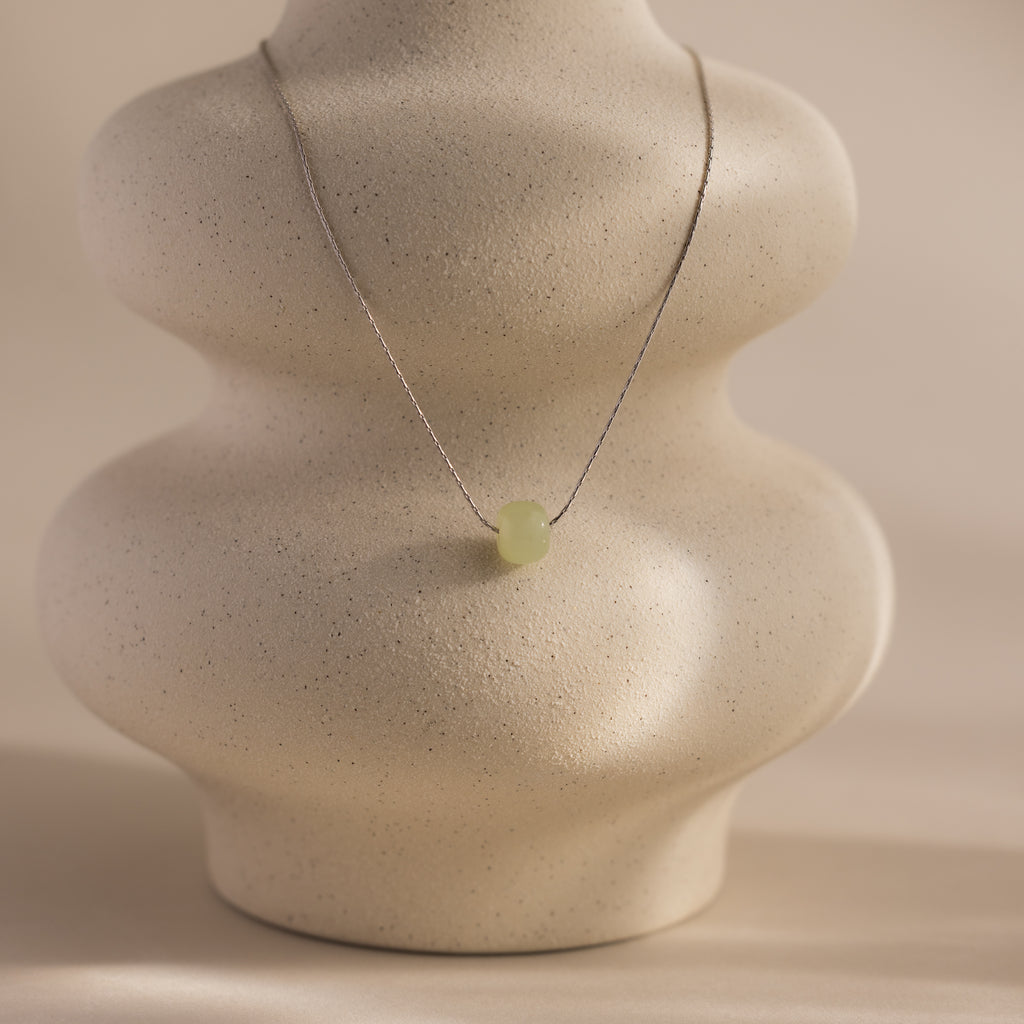 Delicate silver chain necklace featuring a single round green jade bead, displayed on a ceramic prop.