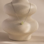 Delicate silver chain necklace featuring a single round green jade bead, displayed on a ceramic prop.