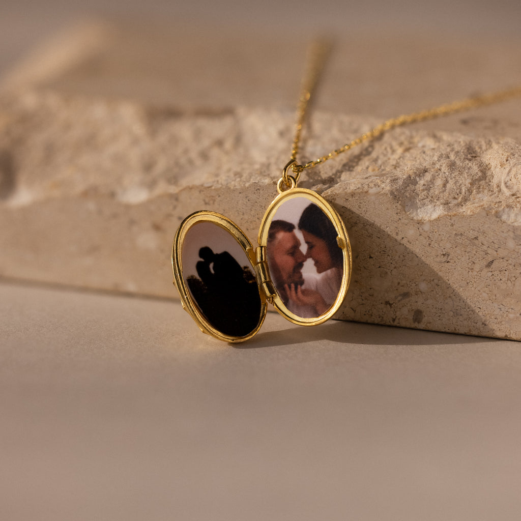 A Floral Handwriting Locket Necklace opens to reveal two couple photos, resting on a stone surface.