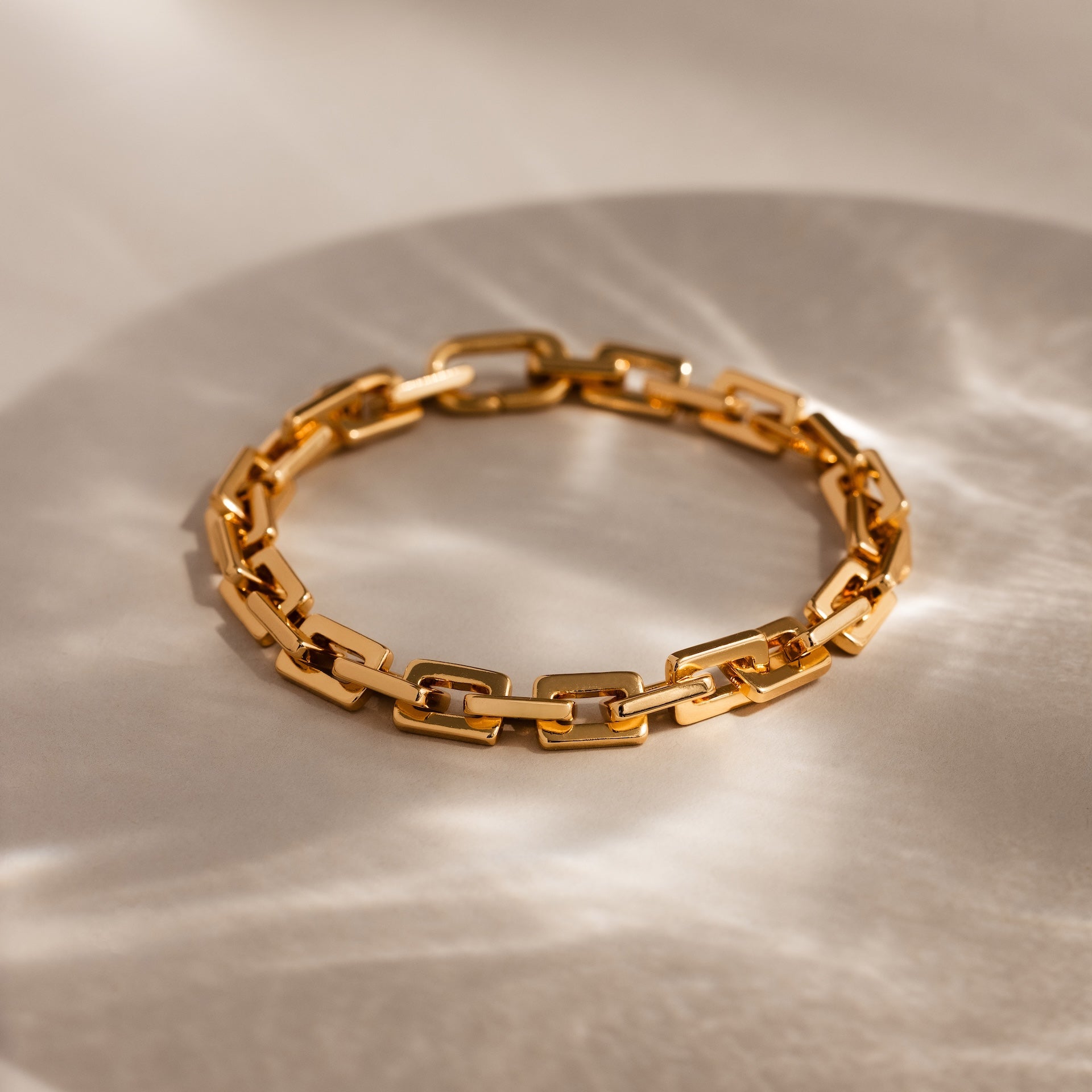 Eternal Link Bracelet in 18K Gold: Features a modern geometric design with rectangular links, presented on a light surface with soft shadows—a must-have contemporary accessory.