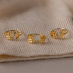 Three Hand & Footprint Duo Name Rings in 18K Gold, featuring unique hand-shaped designs, are beautifully displayed on a beige knitted fabric background—an ideal keepsake gift for new parents.